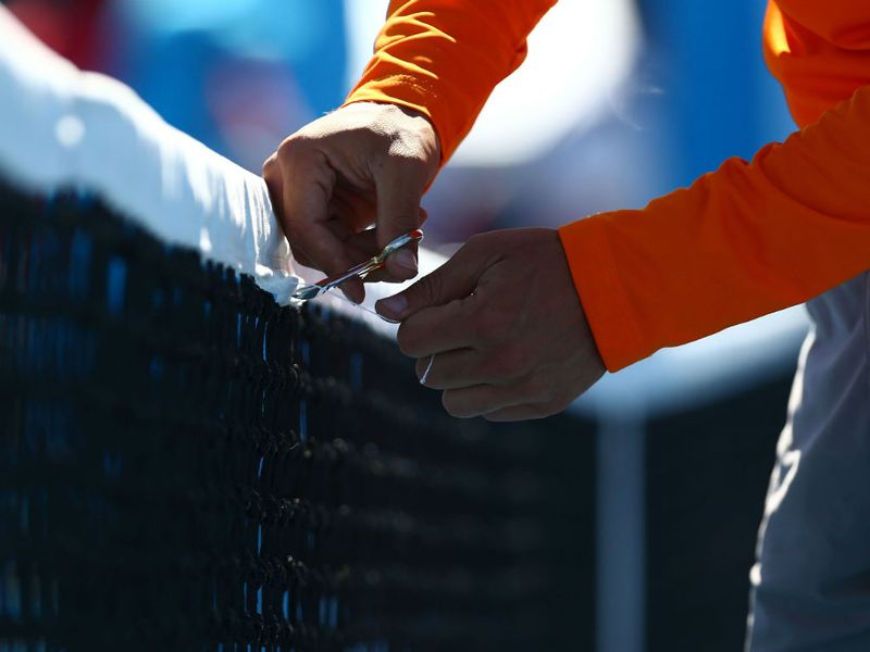 An official makes running repairs to the net during Jamie Baker's game with Lukas Rosol