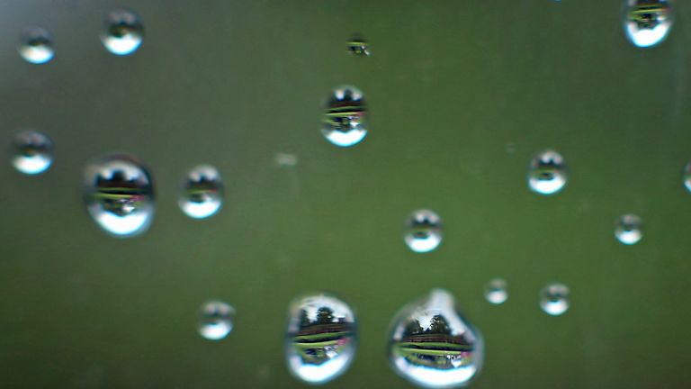 A view of the drenched course is reflected through raindrops on a window