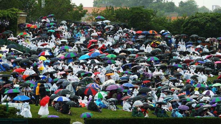 Fans sitting on Murray mound shelter under umbrellas as rain delays the start of play on day six