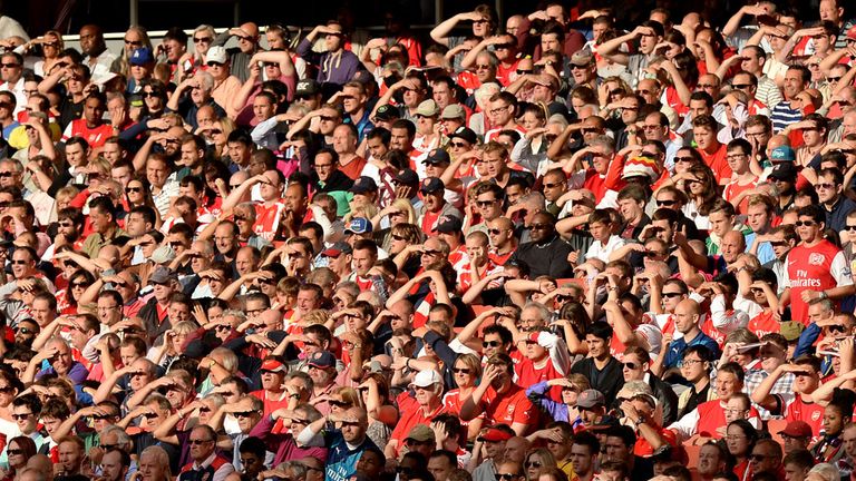 Arsenal fans shield their eyes from the late evening sun in the stands