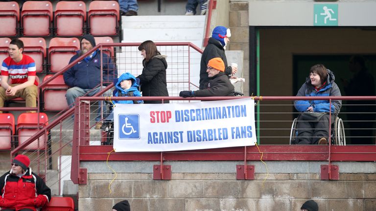 A banner in the stands reads 'Stop Discrimination against disabled fans'