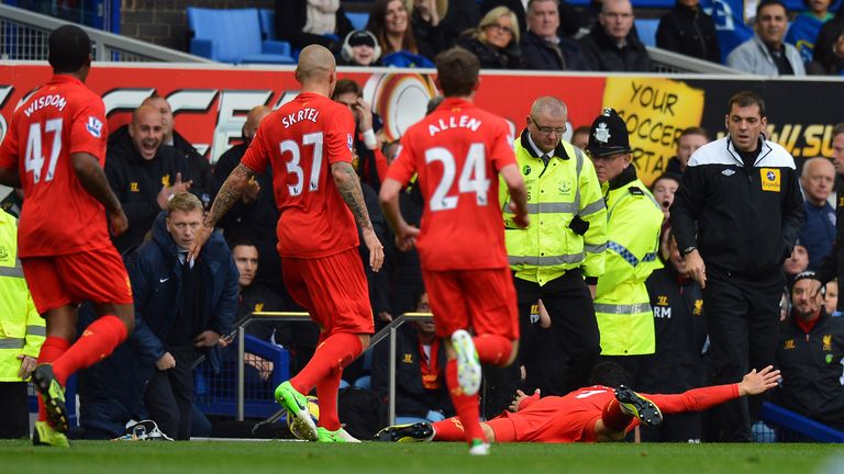 Liverpool striker Luis Suarez celebrates by diving in front of the Everton bench as their manager David Moyes looks on