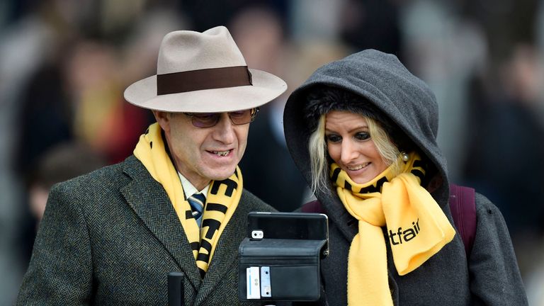 A racegoing couple look at their mobile phone during the Ascot Chase Raceday at Ascot Racecourse.