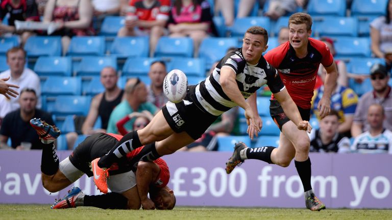 Jack Owens of Widnes Vikings offloads underpressure from Danny Williams and Jake Mullaney of Salford Red Devils