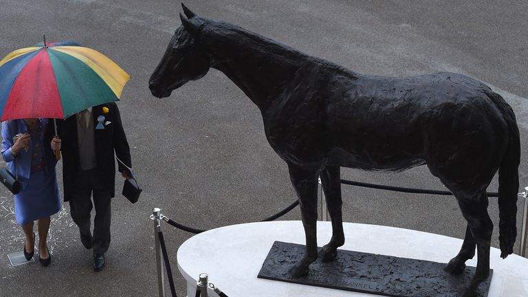 Racegoers walk past the Frankel statue in the rain at Royal Ascot