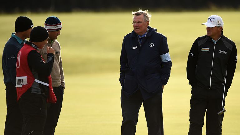 Paul Lawrie of Scotland talks with a rules official on the 13th green as play is suspended due to high winds