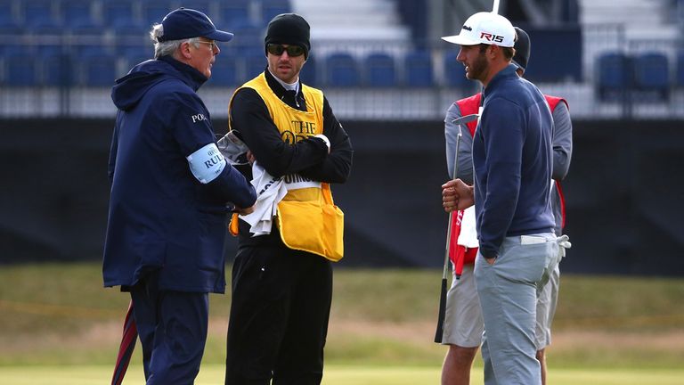 Dustin Johnson of the United States talks with a rules official on the 15th green as play is suspended due to high winds