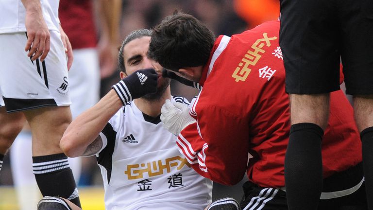 Swansea City's Spanish defender Chico Flores (C) sits injured after a challenge by West Ham United's English striker Andy Carroll (not pictured) during the