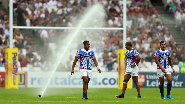 Samoa players look on as the water sprinklers turn on mid-game at the Olympic Stadium