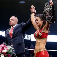 Triple H holds Bayley's hands aloft after her victory