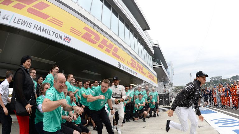 Nico Rosberg runs for cover as Lewis Hamilton sprays the champagne in Mercedes' post-race celebrations