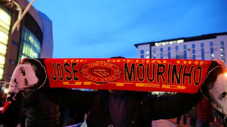 A fan poses with a Manchester United scarf displaying the image and name of former Chelsea manager Jose Mourinho