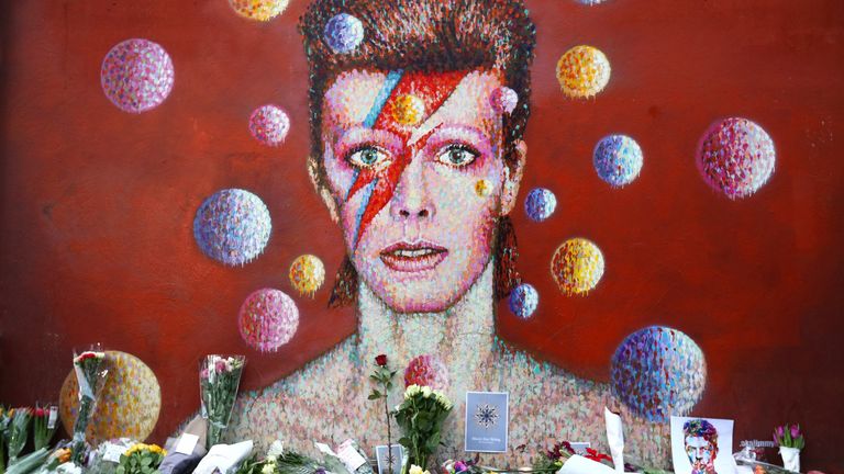 LONDON, ENGLAND - JANUARY 11: Flowers are laid beneath a mural of David Bowie in Brixton on January 11, 2016 in London, England. British music and fashion 