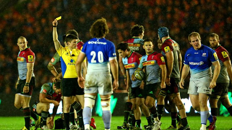 Referee Craig Maxwell-Keys shows a yellow card to Rhys Gill of Saracens (right in blue) which was later upgraded to red