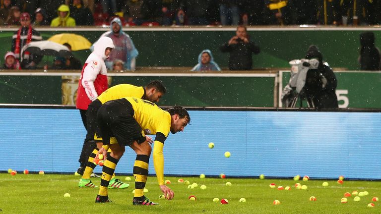 Players remove tennis balls thrown by Dortmund fans from the pitch 