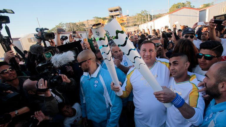 Syrian refugee athlete Ibrahim Al-Hussein (R) receives the Olympic flame from the head of Greece's Olympic Committee, Spyros Caprolas