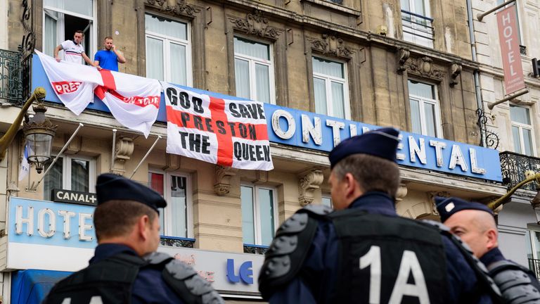 Police officers stand on guard as England fans hang flags from their hotel balcony in central Lille, on 15 June 2016