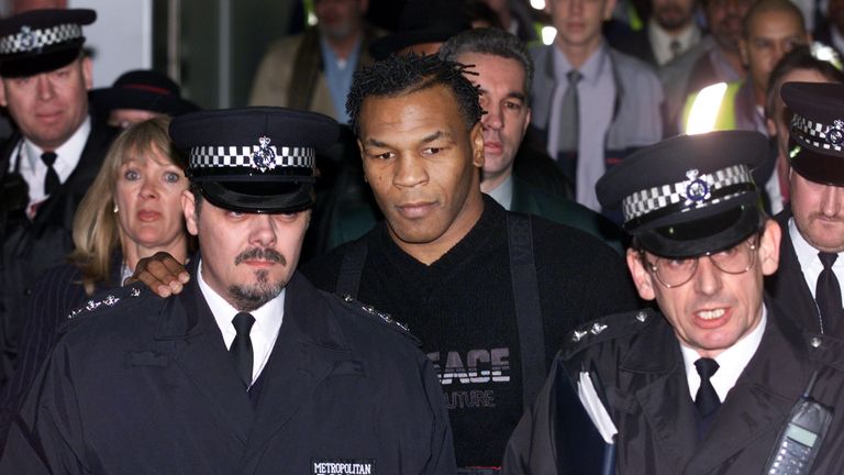 Former world heavyweight champion Mike Tyson (C) is guided through the arrival terminal by police officers as he arrives at Heathrow Airport 16 January 200