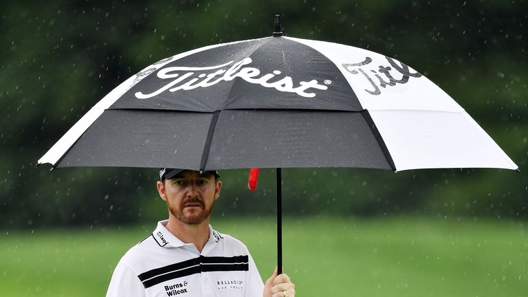 Jimmy Walker of the United States walks under an umbrella in the rain 