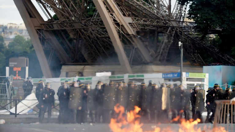 French riot policemen stand near a fire during clashes near the fan zone of the Champs de Mars next to the Eiffel tower in Paris on July 10, 2016 during th