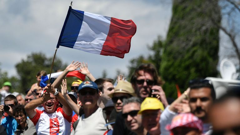 A man waves a French national flag as he cheers with other fans along the road during the 178 km twelvelth stage of the 103rd edition of the Tour de France