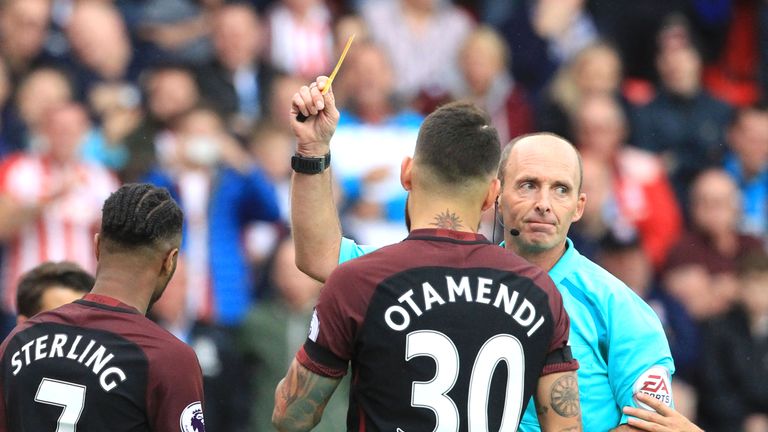 Referee Mike Dean (R) shows Raheem Sterling (L) a yellow card