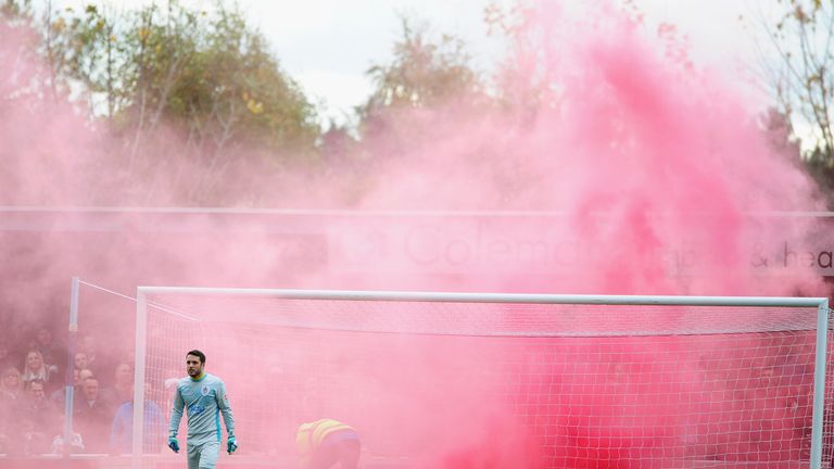 Lloyd Irish of Taunton Town looks on as a flare is thrown onto the pitch