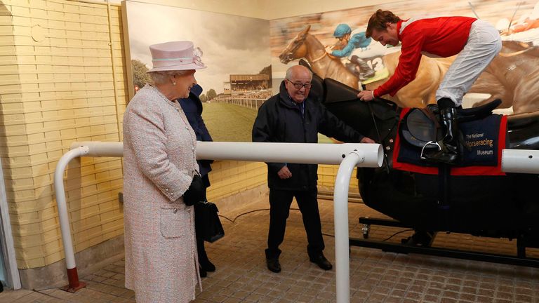 Queen Elizabeth II watches jockey Pat Cosgrave on a simulator during a visit to the National Heritage Centre for Horseracing