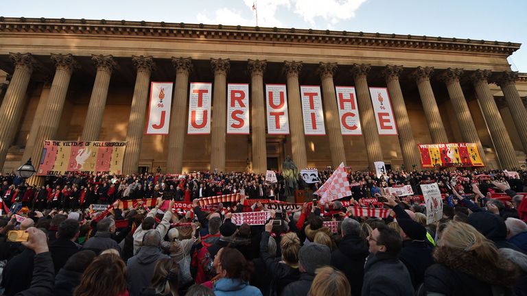 People hold Liverpool football scarves in the air as they sing "You'll Never Walk Alone" outside St George's Hall in Liverpool