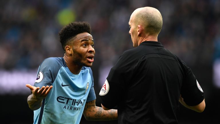 Mike Dean shows Raheem Sterling of Manchester City a yellow card t