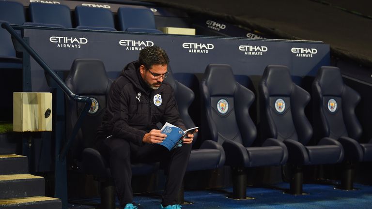 MANCHESTER, ENGLAND - MARCH 01:  David Wagner manager of Huddersfield Town sits on the team bench as he reads the match day programme prior to The Emirates