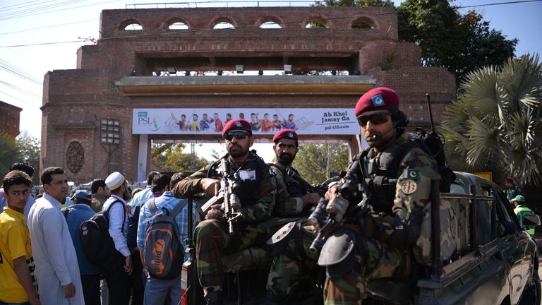 Pakistani soldiers sit in a vehicle as they patrol while cricket fans queue at an entry gate of The Gaddafi Cricket Stadium in Lahore