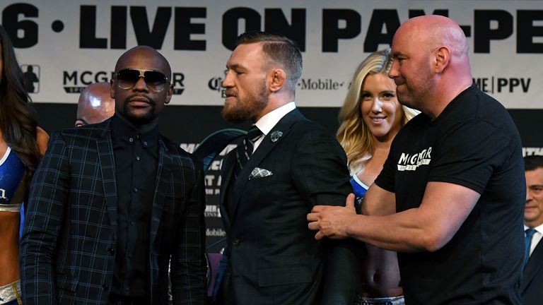 Floyd Mayweather poses as Conor McGregor is pulled back by UFC President Dana White