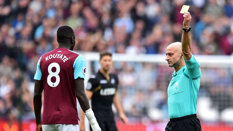 Referee Roger East shows a yellow card to West Ham United's Senegalese midfielder Cheikhou Kouyate (L)