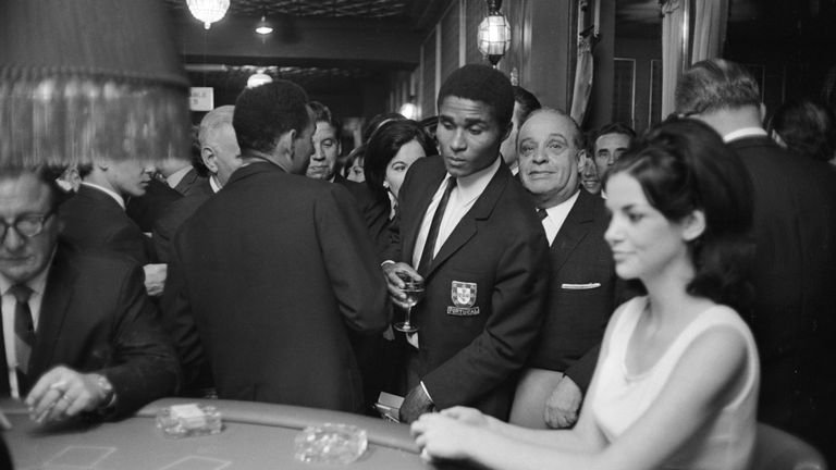 Portuguese striker Eusebio looks over at a game of blackjack in a sporting club in Kensington after the 1966 World Cup in England