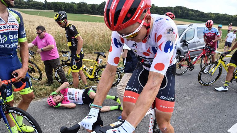 Simon Clarke lies on the road as Tom Skujins gets back on his bike after a bad crash 17km from the end