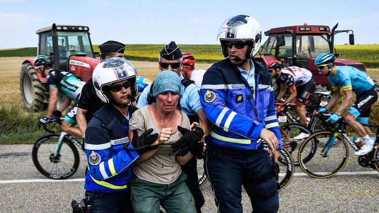 Police restrain a protester as stage 16 is paused while riders get medical attention