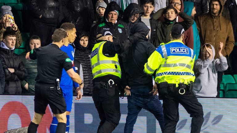 A Hibs fan is led away by police after running onto the pitch to confront Rangers captain James Tavernier