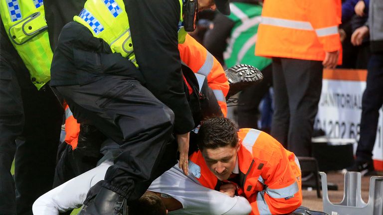 A Newcastle United fan is removed from the pitch by stewards and police