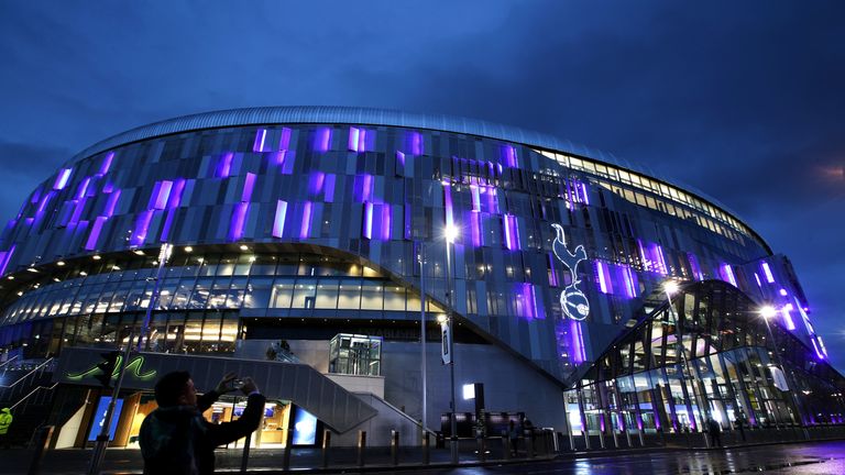 A passer-by takes a photo outside an illuminated Tottenham Hotspur Stadium