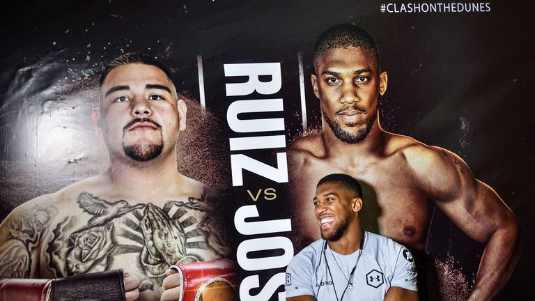 Anthony Joshua poses before a poster of the upcoming "Clash on the Dunes" heavyweight rematch with Andy Ruiz Jr