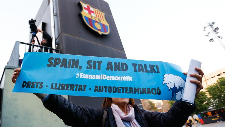 A woman holds up a banner with the words 'Tsunami Democratic' and 'Spain, Sit and Talk!' before the Liga match between Barcelona and Real Madrid