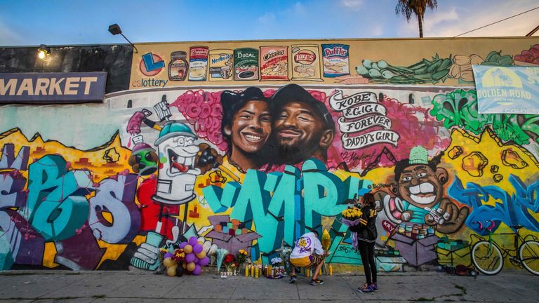 Members of the public light a candle and lay flowers below a mural of Kobe Bryant and his daughter Gianna Bryant by the artists Muck Rock and Mr79lts