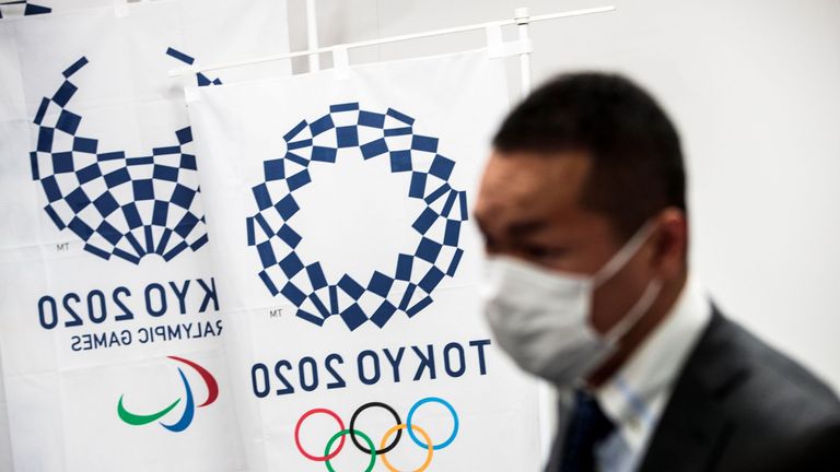 A man wearing a face mask walks past banners of the Tokyo Olympic Games during a Tokyo 2020 press conference about the coronavirus pandemic