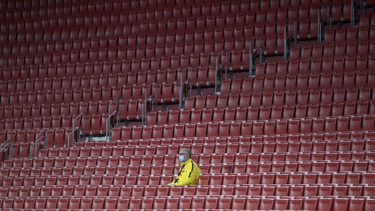 A stadium worker wearing a face mask sits amid empty spectator seats during the Spanish League football match between Sevilla FC and Real Betis at the Ramon Sanchez Pizjuan stadium in Seville on June 11, 2020. 