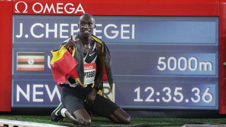 Uganda's Joshua Cheptegei, wearing an Uganda national flag on his shoulders, poses for pictures next to the timer screen after breaking the world record in the men's 5000metre event during the Diamond League Athletics Meeting at The Louis II Stadium in Monaco on August 14, 2020
