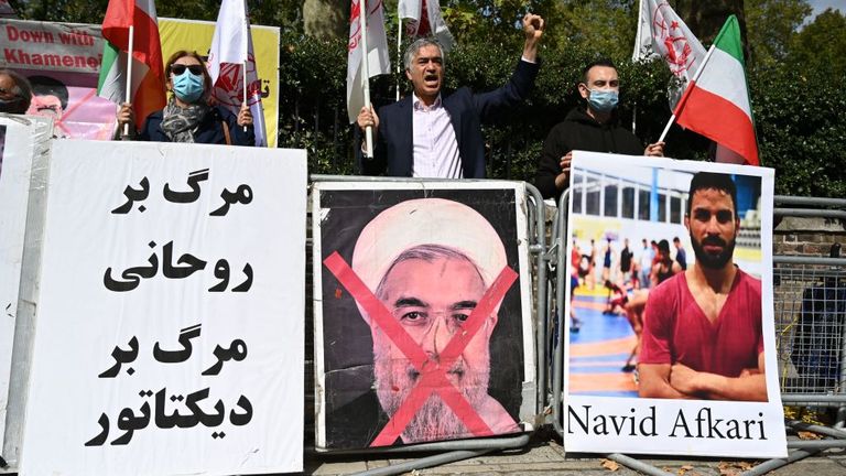 Protesters wave the Lion and Sun flag of the National Council of Resistance of Iran and the white flag of the People's Mujahedin of Iran, two Iranian opposition groups, with a placard depicting the crossed out face of Iran's President Hassan Rouhani as they demonstrate outside the Iranian embassy in London.