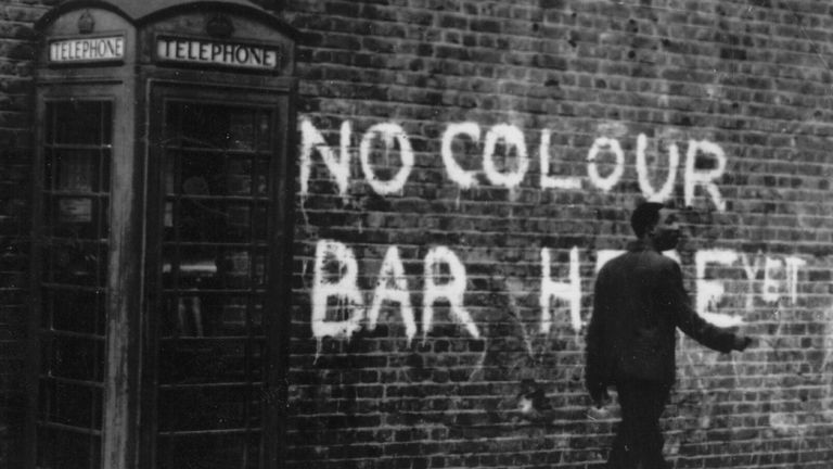 circa 1959: A black man walking down a Notting Hill Street, where race riots had recently taken place. The graffiti behind him reads, 'No Colour Bar Here - Yet'. (Photo by Keystone/Getty Images)
