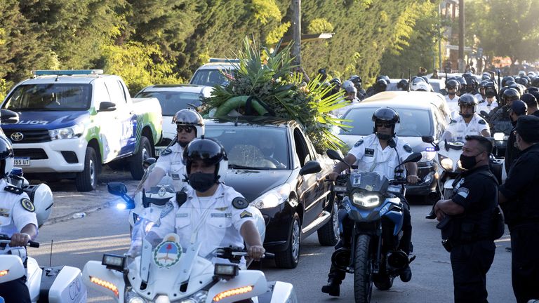 A flower car leads Diego Maradona's hearse into the cemetery ahead of his private burial 