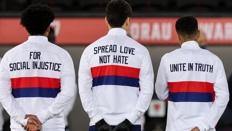 美国运动员在奏国歌时排成一队，他们的训练上衣背面印着反种族主义的信息
